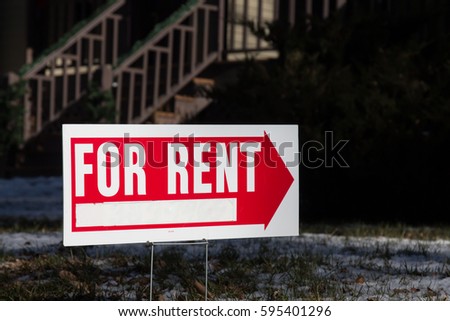 Red for rent sign in front of a dark home with wooden steps
