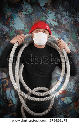 portrait of a man in a red helmet and a black t-shirt with a hose in his hands on a gray background studio