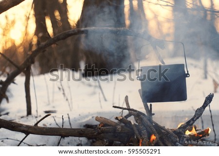 A pot in the fire, water is heated in the winter forest a