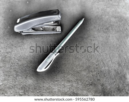 A stapler with a pen on a gray background