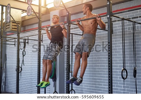 Gym partners buddies doing pull ups in a industrial looking gym, muscular fit lean men exercising Royalty-Free Stock Photo #595609655