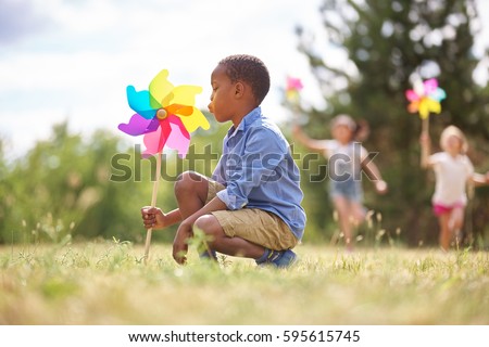 African boy and friends with pinwheels playing at the park Royalty-Free Stock Photo #595615745