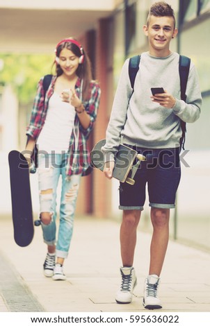 Attractive young friends carrying skateboards and walking through city