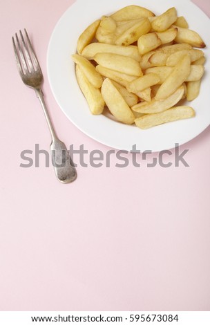 A bowl of French fries on a pastel pink background, with fork and empty space below