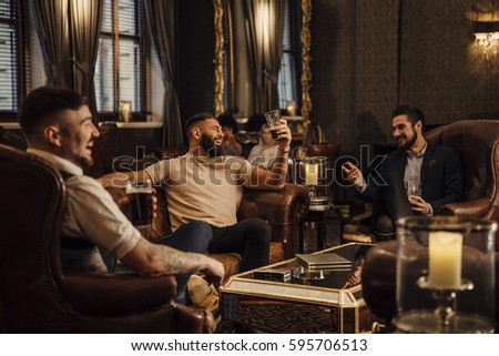 Three men are enjoying drinks in a bar lounge. They are talking and laughing while drinking pints of beer.  Royalty-Free Stock Photo #595706513