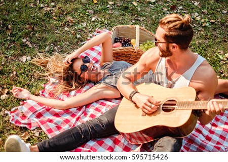 Man playing guitar to his girl on a picnic