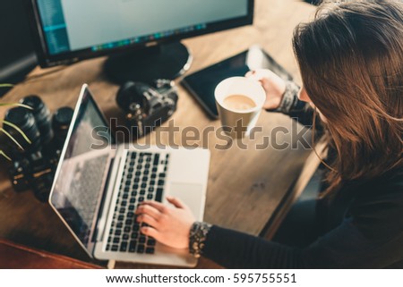Young woman photographer editing pictures in a photographic studio drinking coffe