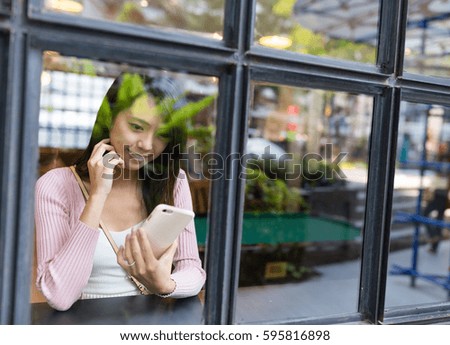 Window reflection of woman use of mobile phone inside coffee shop
