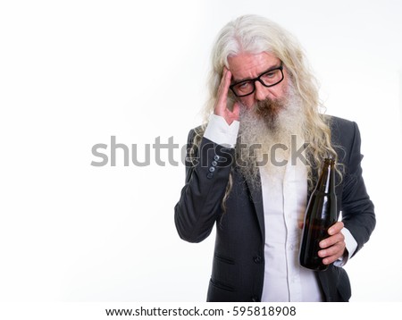 Studio shot of senior bearded businessman holding bottle of beer and looking tired