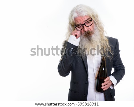 Studio shot of sad senior bearded businessman holding bottle of beer while crying