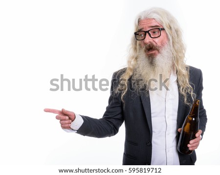 Studio shot of senior bearded businessman holding bottle of beer and pointing to the side