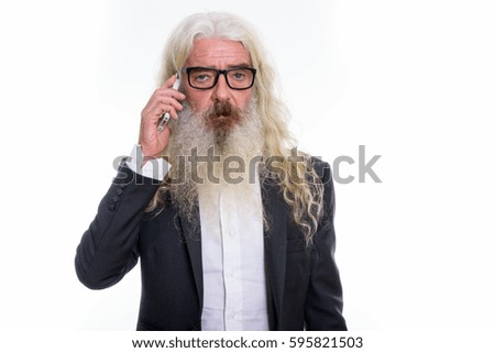 Studio shot of senior bearded businessman talking on mobile phone