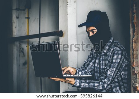 computer hacker of terrorist stealing information with laptop in abandoned building. Low key photo.