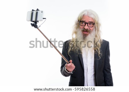 Studio shot of happy senior bearded businessman smiling while taking selfie picture with mobile phone on selfie stick