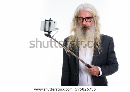 Studio shot of senior bearded businessman taking selfie picture with mobile phone on selfie stick