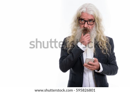 Studio shot of senior bearded businessman thinking while holding mobile phone