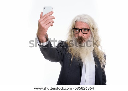 Studio shot of senior bearded businessman taking selfie picture with mobile phone