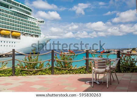 Table on patio of a coastal Caribbean restaurant with a luxury cruise ship in the background