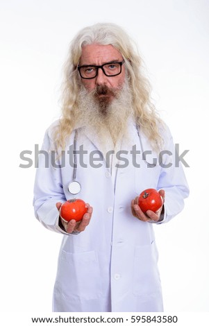 Studio shot of senior bearded man doctor holding two red tomatoes