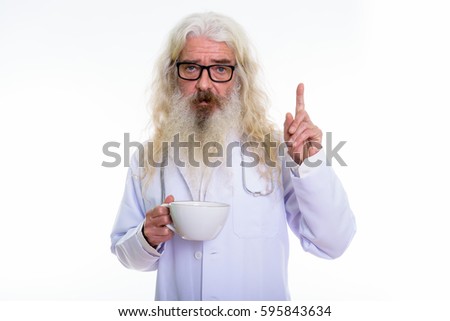 Studio shot of senior bearded man doctor holding coffee cup and pointing finger up