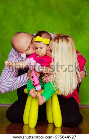 Mom and dad kiss their little daughter's cheeks while she sits on yellow chair
