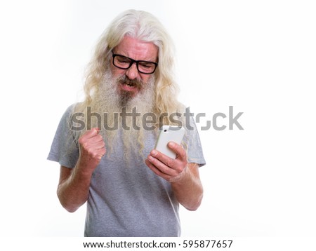 Studio shot of senior bearded man using mobile phone while looking angry
