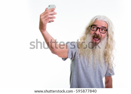 Studio shot of happy senior bearded man smiling while taking selfie picture with mobile phone