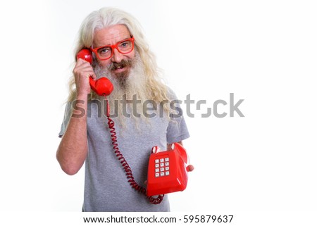 Studio shot of happy senior bearded man smiling while talking on old telephone
