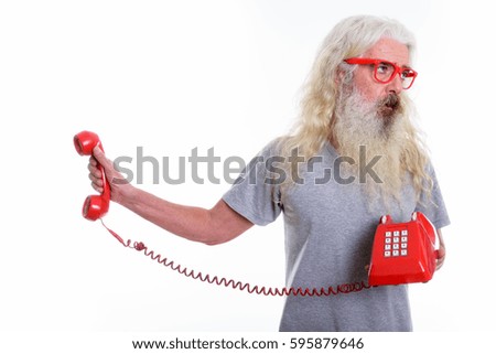 Studio shot of senior bearded man holding old telephone while looking away and annoyed