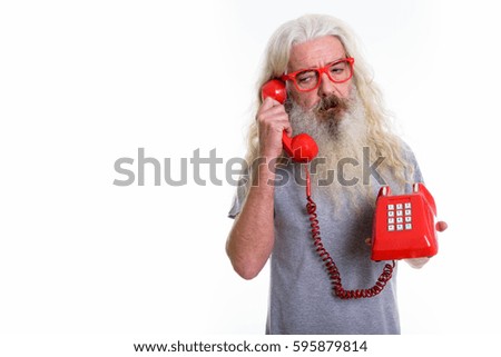 Studio shot of senior bearded man looking tired while talking on old telephone