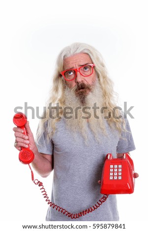 Studio shot of senior bearded man thinking and looking up while holding old telephone