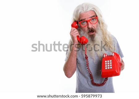 Studio shot of senior bearded man looking shocked while talking on old telephone