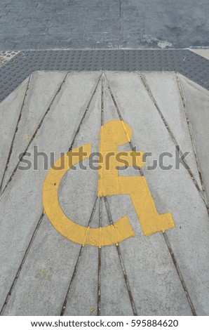 Yellow handicap sign to indicate the way of disable people on concrete road