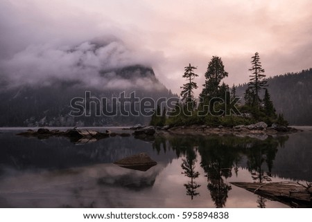 Morning landscape view on a reflection in the water with an island surrounded by mountains. Picture taken North of Vancouver in Widgeon Lake, British Columbia, Canada, during a cloudy sunrise.