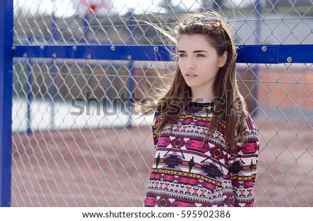 Outdoor portrait of young pretty girl with windy hair near the basketball court, wearing stylish clothes