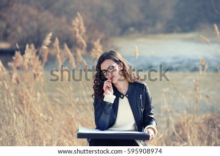 Beautiful girl draws on paper by the river
