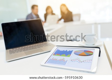 Digital tablet showing data chart on screen and blank screen of laptop computer at business meeting room 
