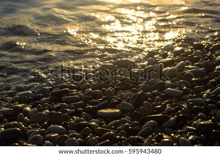 sea pebble beach with multicoloured stones, transparent waves with foam, on a warm evening