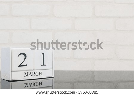 Closeup white wooden calendar with black 21 march word on black glass table and white brick wall textured background with copy space , selective focus at the calendar