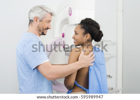 Smiling Doctor Looking At Female Patient Undergoing Mammogram Test Royalty-Free Stock Photo #595989947