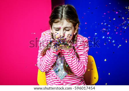 A little girl with pigtails blows out confetti.