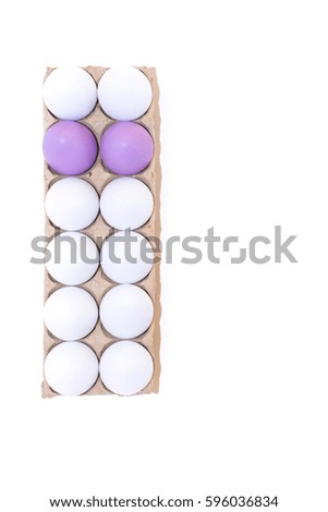 Two Easter eggs dyed lavender and ten white hard boiled hen's eggs in a cardboard carton photographed from above against a white background with copy space.