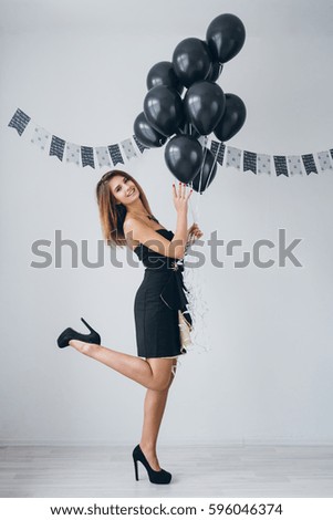 Young beautiful girl in a black dress with black balloons. Toning.