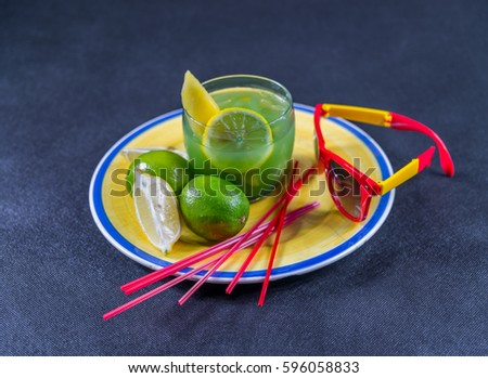 colored drink, a combination of blue and green, decorated with lemon and melon, a glass, a piece of lemon and two limes, yellow and red sunglasses, yellow plate