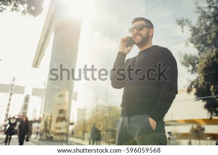 Young business man standing in front his office building.Handsome successful entrepreneur going on a coffee/lunch break.Casual friday.Talking on the phone,communicating with partners.Freelancer