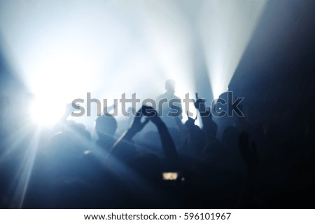 Blurred silhouettes of people at a concert in front of the scene in bright light