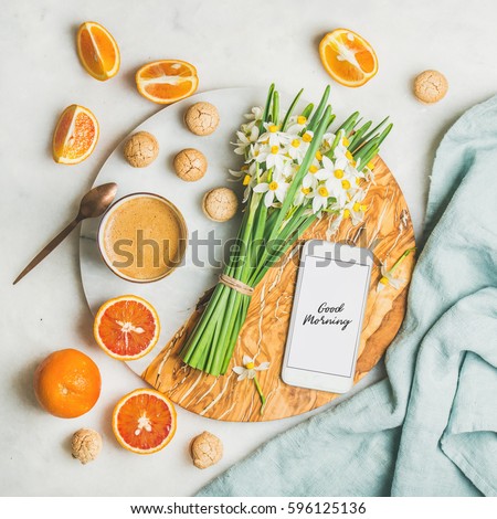 Cup of morning coffee, cookies, red oranges, bucket of spring flowers and mobile phone with text Good morning on board over light grey marble background, top view. Morning greeting card concept