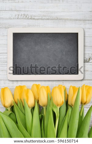 Yellow tulips with chalkboard over shabby white wooden background, top view