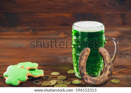 Beautiful background for St. Patrick's day with a glass of green beer, gold coins and a horseshoe on a wooden table. Free space.