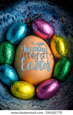 Happy Easter 2017 lettering on egg lined with small chocolate eggs wrapped in colorful foil. Vertical image
